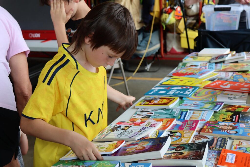 Young boy looks at new books on a table, determining which one he'd like to take home.