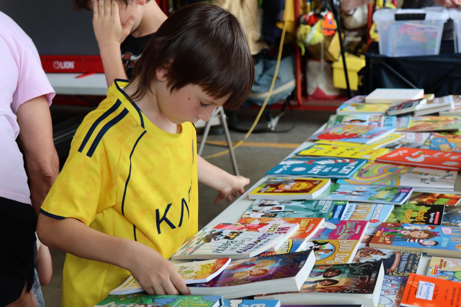Young boy looks at new books on a table, determining which one he'd like to take home.