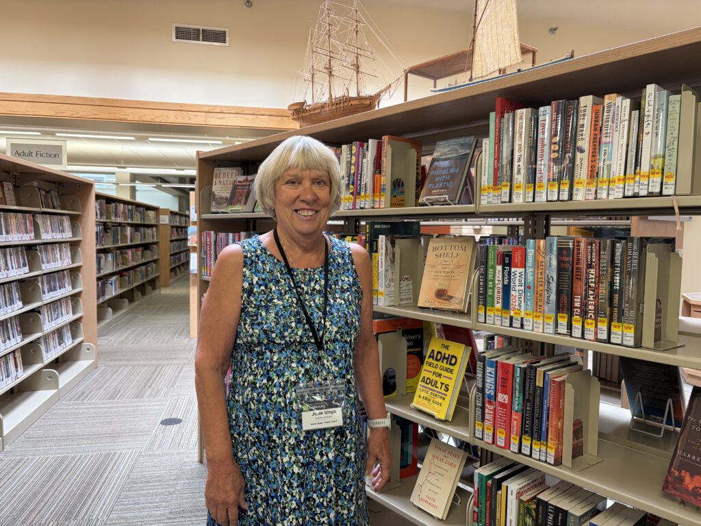 Julie Ungs stands by a book shelf inside the Nevada Public Library.
